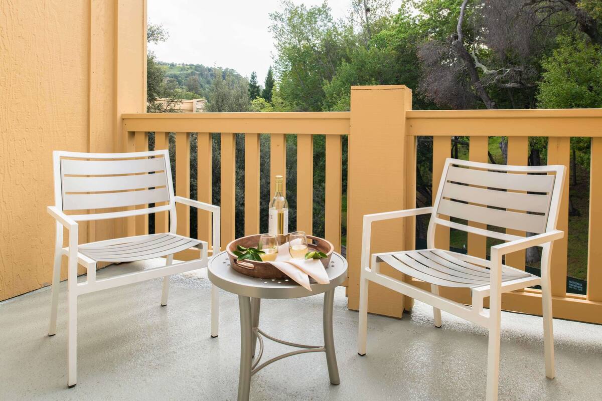 A balcony with two white chairs and a small table, a bottle, and glasses.