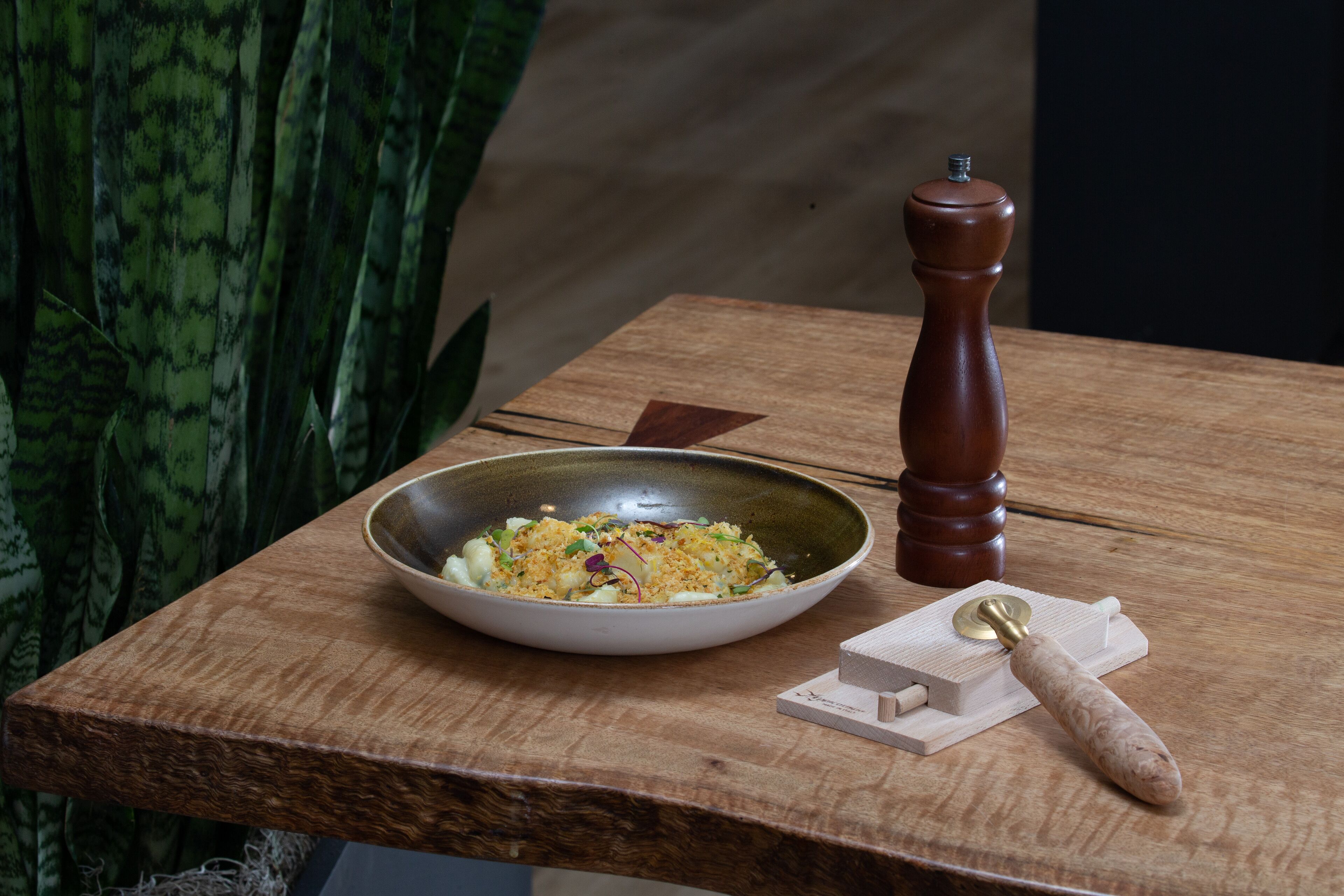 A wooden table with a bowl of food, a pepper grinder, and a corkscrew.