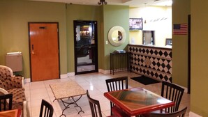 A hotel lobby with a reception desk, a dining area with a glass-top table and chairs, a small rug, and a chandelier. - Budgetel Inn & Suites (Augusta)