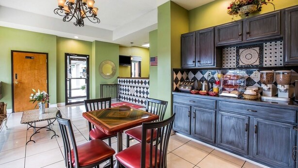 A dining area with a table and chairs, a chandelier, and a kitchen area with cabinets and a countertop. - Budgetel Inn & Suites (Augusta)