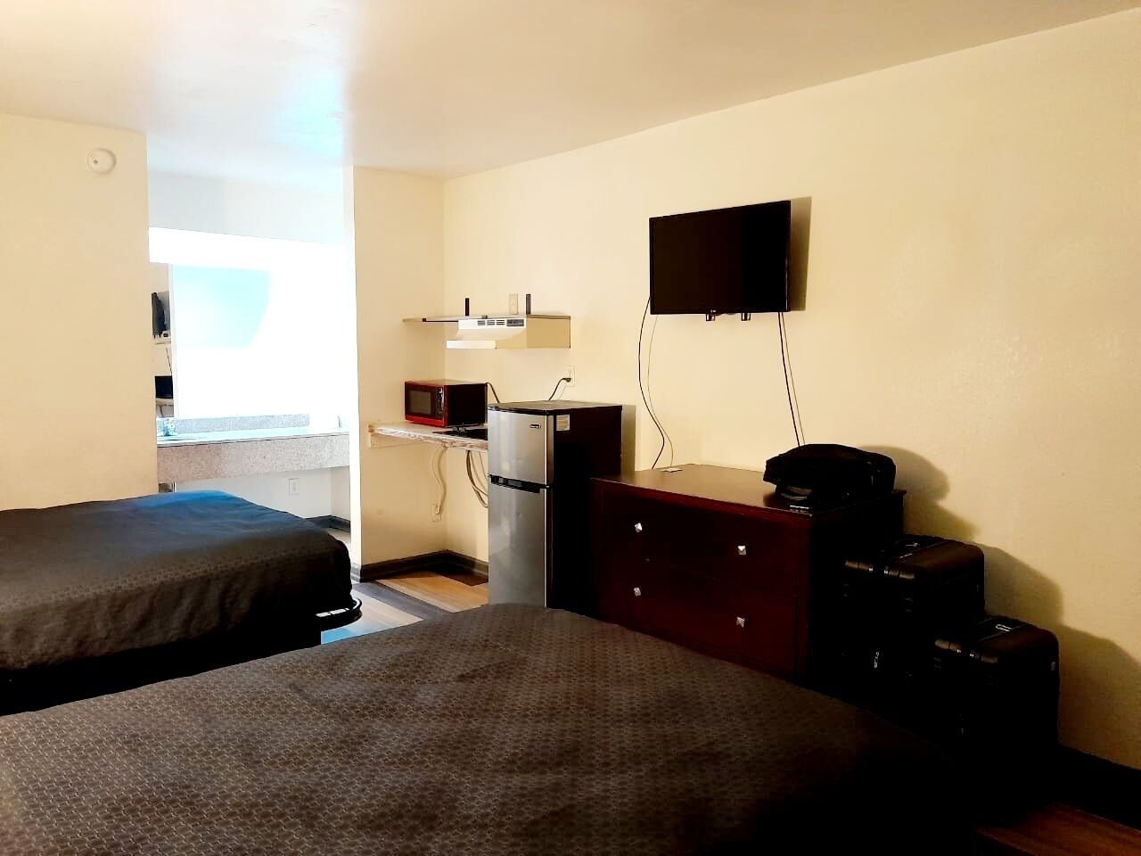A hotel room with two beds, a desk, a microwave, a refrigerator, a TV, and a dresser.