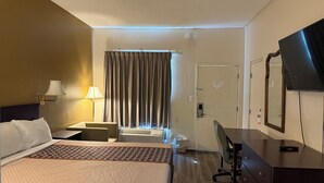 A hotel room with a large bed, a desk, a chair, a TV, and a window with curtains. - Budgetel Inn & Suites (Augusta)