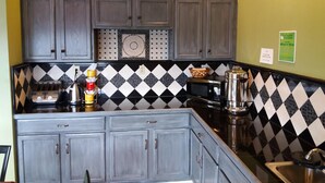 A kitchen with grey cabinets, a black and white checkered backsplash, a toaster, a kettle, a microwave, and a coffee maker. - Budgetel Inn & Suites (Augusta)