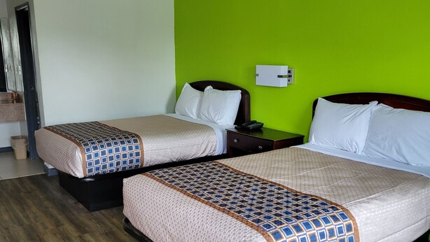 A hotel room with two beds, each with a patterned bedspread, a bedside table with a phone, and a green wall. - Budgetel Inn & Suites (Augusta)
