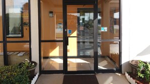 A hotel entrance with a glass door, a small outdoor seating area with potted plants, and a visible parking sign. - Budgetel Inn & Suites (Augusta)