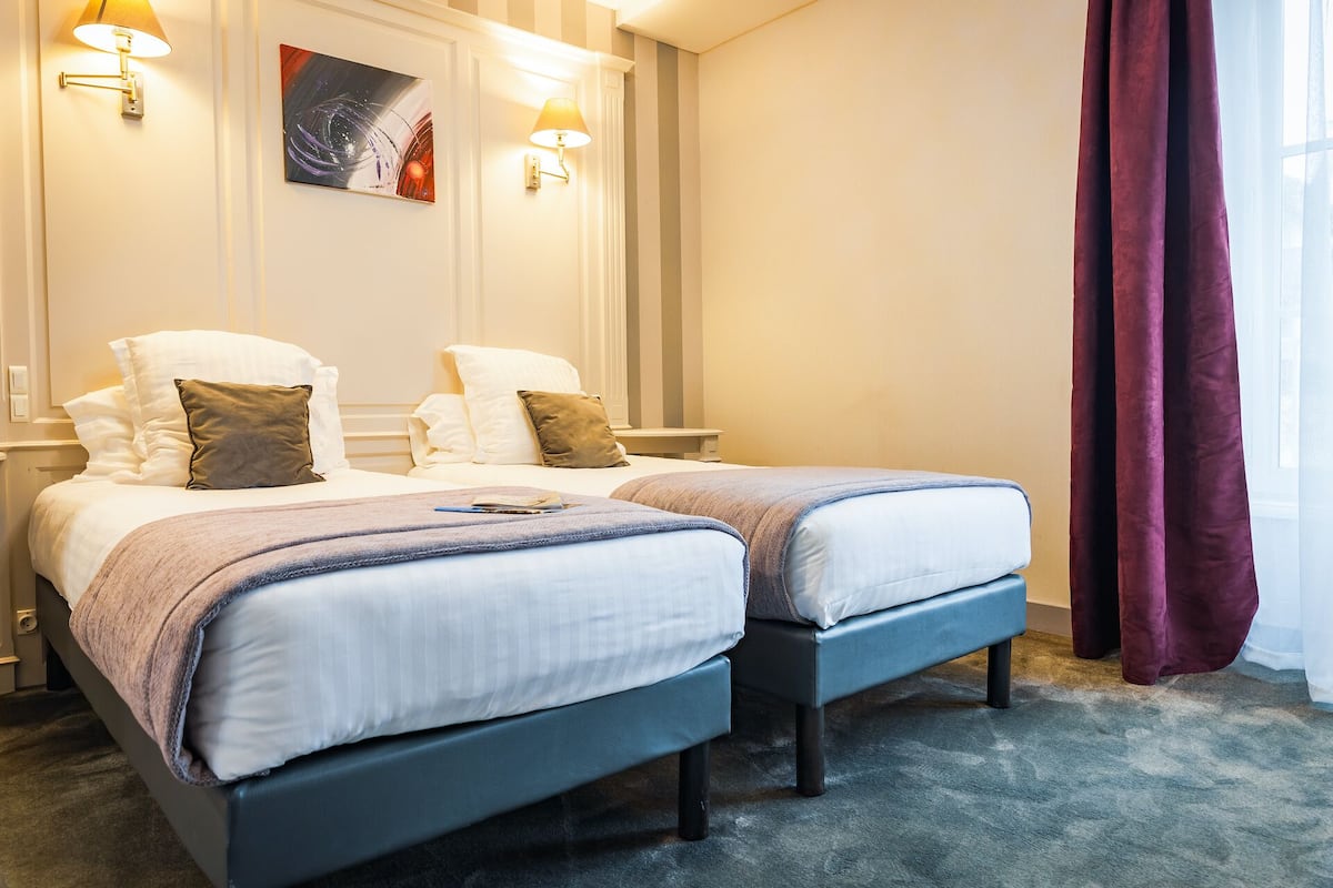 Une chambre d’hôtel avec deux lits, un tableau au mur et une fenêtre avec des rideaux.
