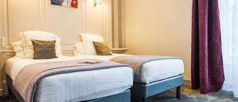 A hotel room with two beds, a painting on the wall, and a window with curtains.
