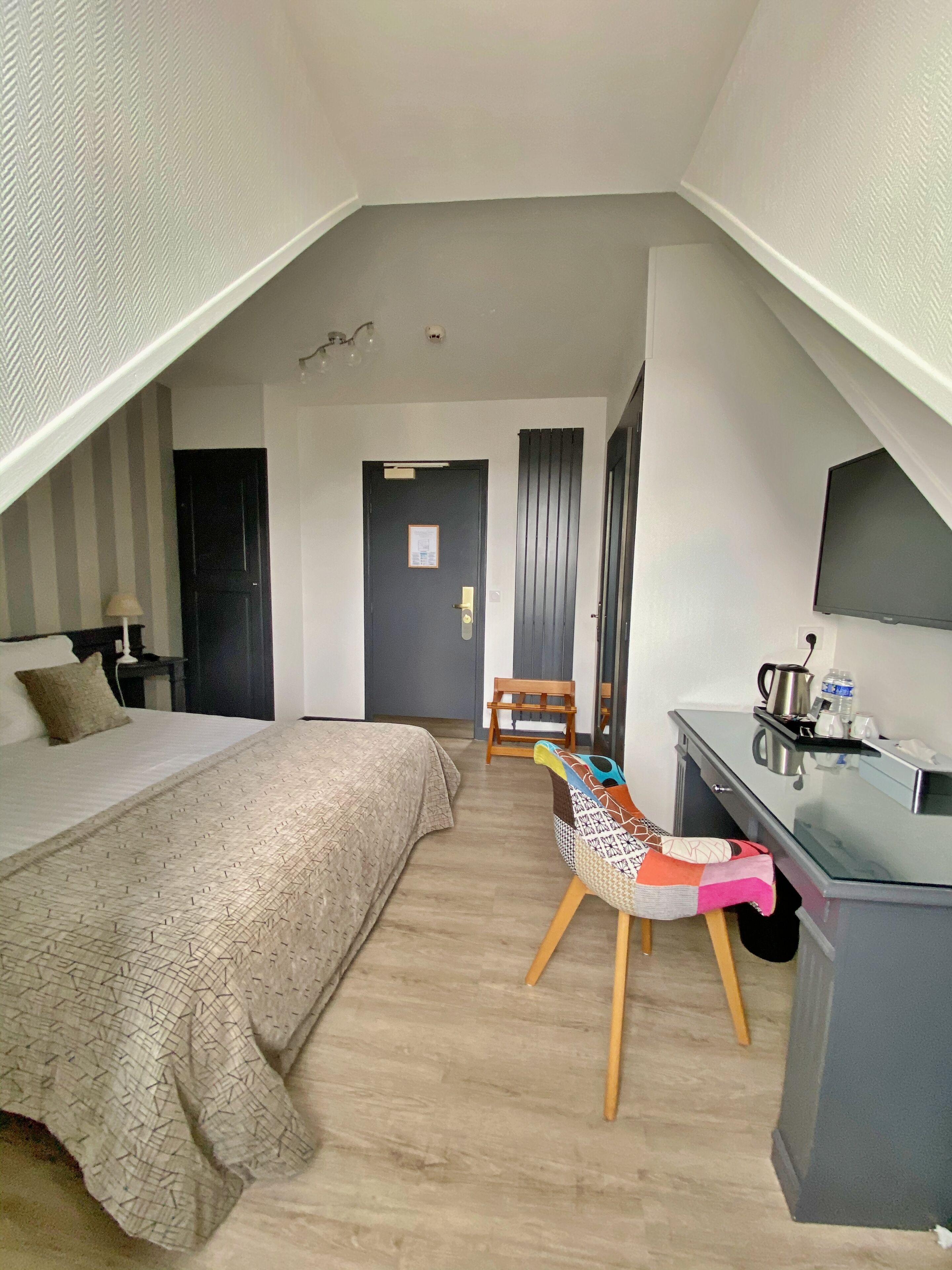 Una habitación de hotel con una cama, un escritorio, una silla, un televisor y una puerta.