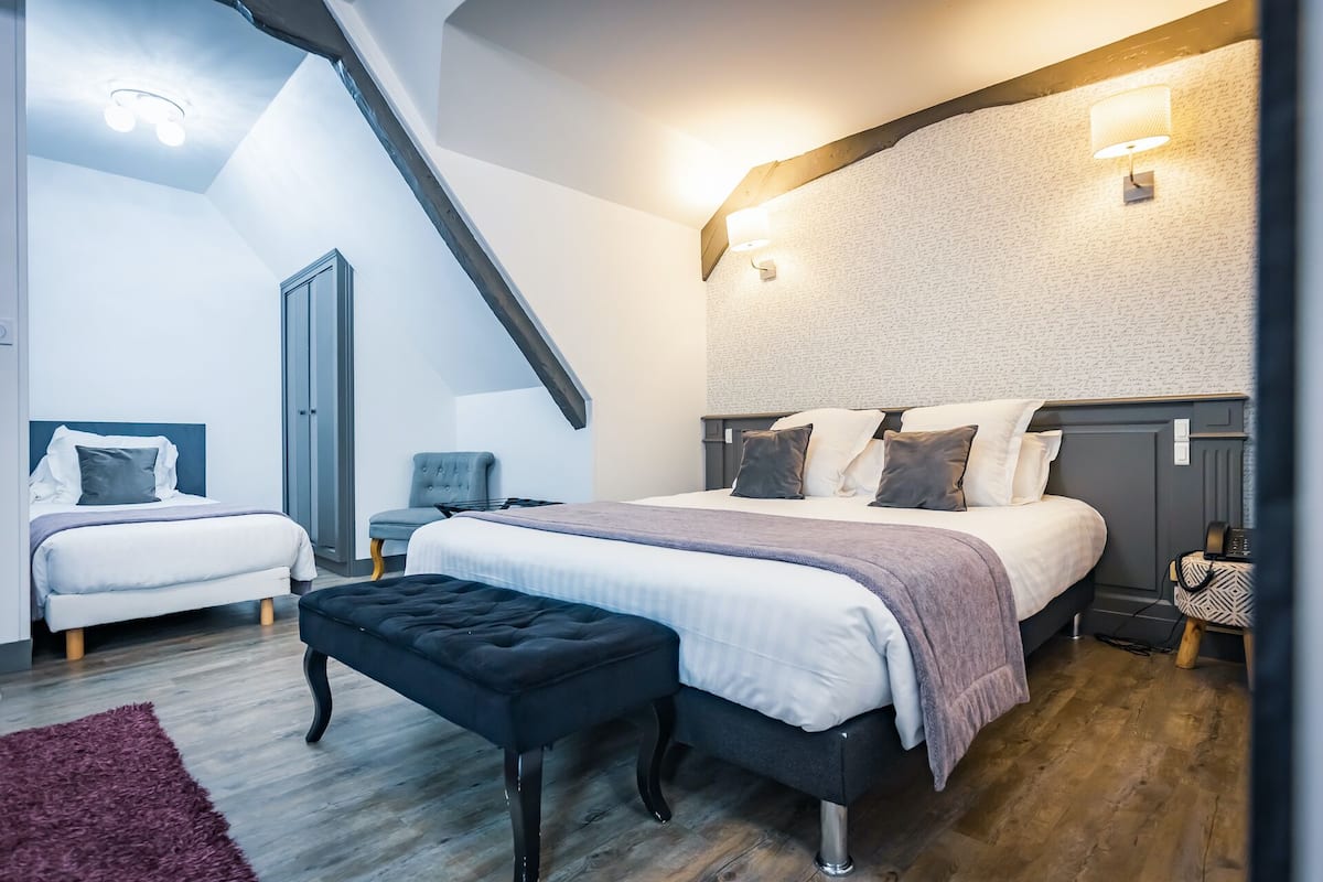 Une chambre moderne avec un grand lit, deux petits lits, un banc et un bureau.