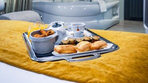A hotel room with a bed, a tray of breakfast items including croissants, a cup, and a glass of orange juice.