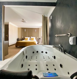 Una habitación de hotel moderna con una bañera grande, una cama con ropa de cama amarilla y un área de baño separada.