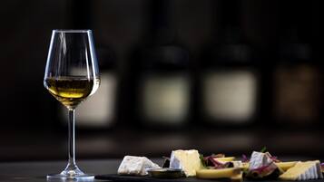 A wine glass with a white wine, a cheese board with various cheeses and accompaniments, and blurred bottles in the background.