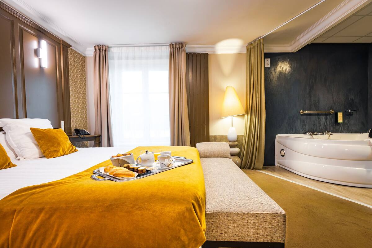 Une chambre d’hôtel avec un lit, un banc, un plateau de petit-déjeuner, une lampe et une baignoire.