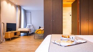 A hotel room with a bed, a TV, a desk, and a bathroom visible through an open door.