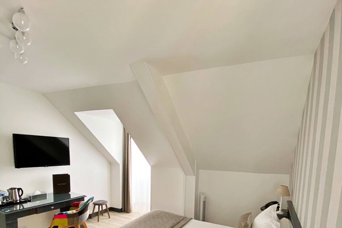 Une chambre d’hôtel moderne dotée d’un grand lit, d’un bureau avec un téléviseur à écran plat, d’une chaise et d’une lampe.