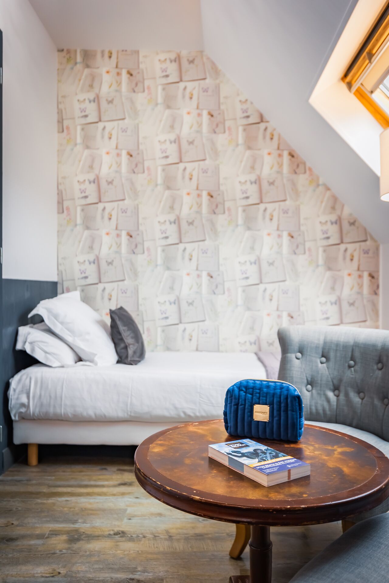 Una habitación acogedora con una cama, un sofá gris, una mesa redonda de madera con un libro y una pared decorada con motivos de mariposas.