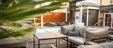 A covered outdoor seating area with a pool, lounge chairs, and a table.