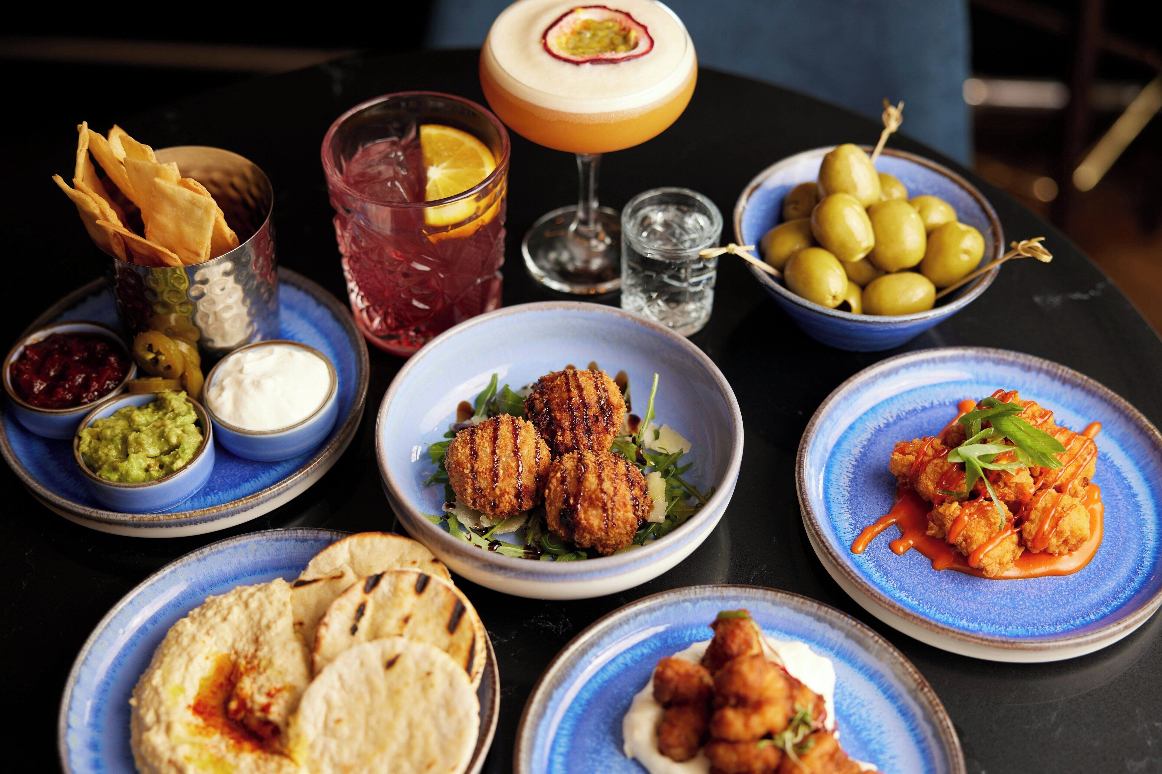 A table with various dishes, drinks, and bowls of olives and dips.