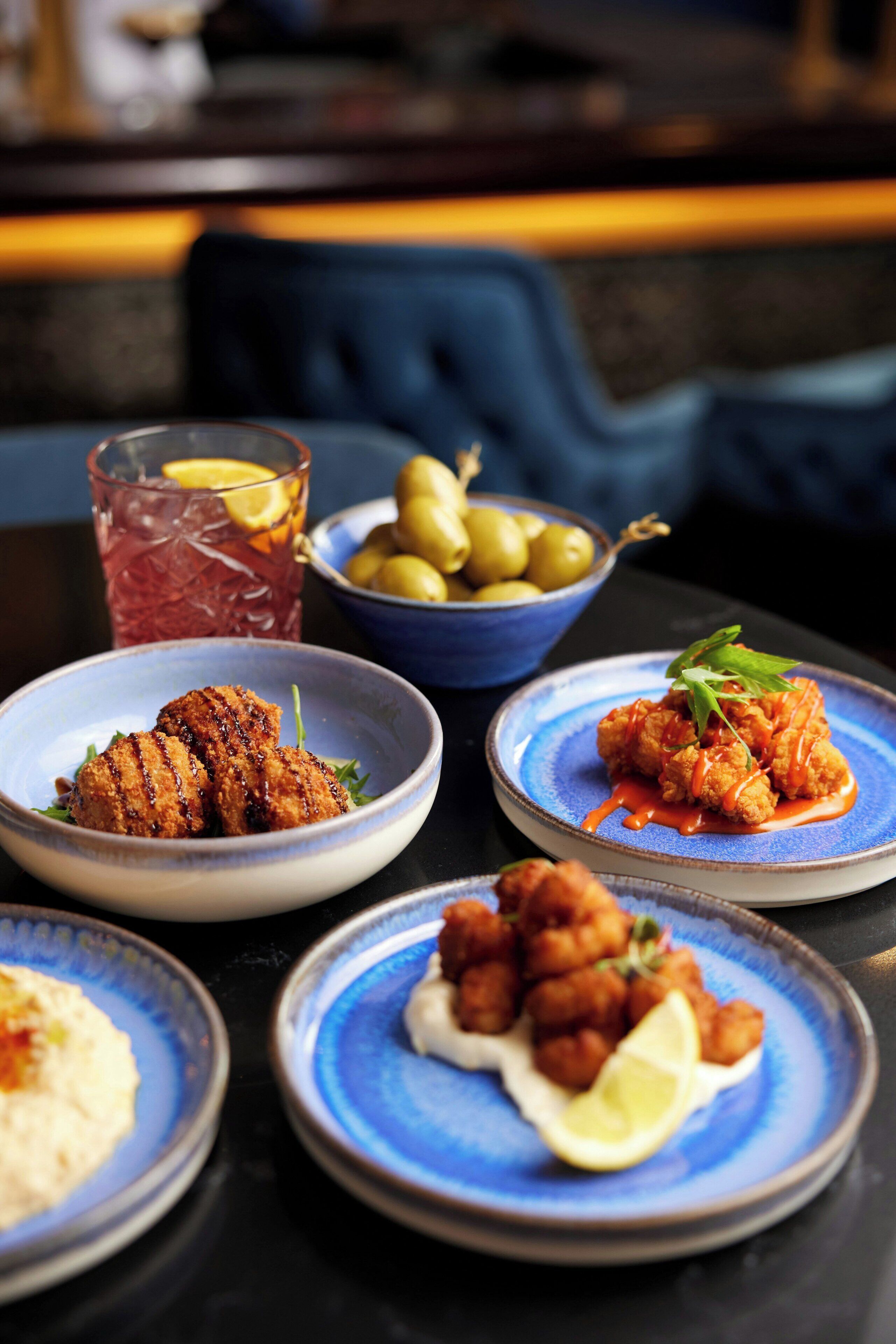 A table with plates of food, a bowl of olives, and a glass of drink.
