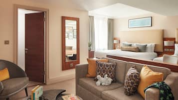 A hotel room with a sofa, a small table with books, a bed with a headboard, and a large mirror.