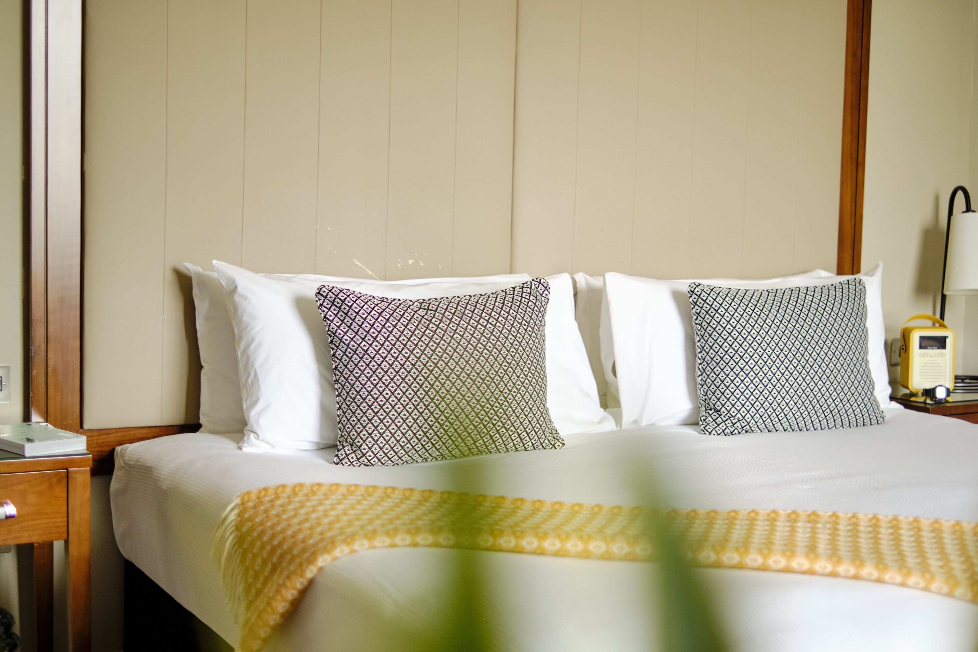 Habitación de hotel con cama, dos almohadas estampadas, mesita de noche con lámpara y teléfono.