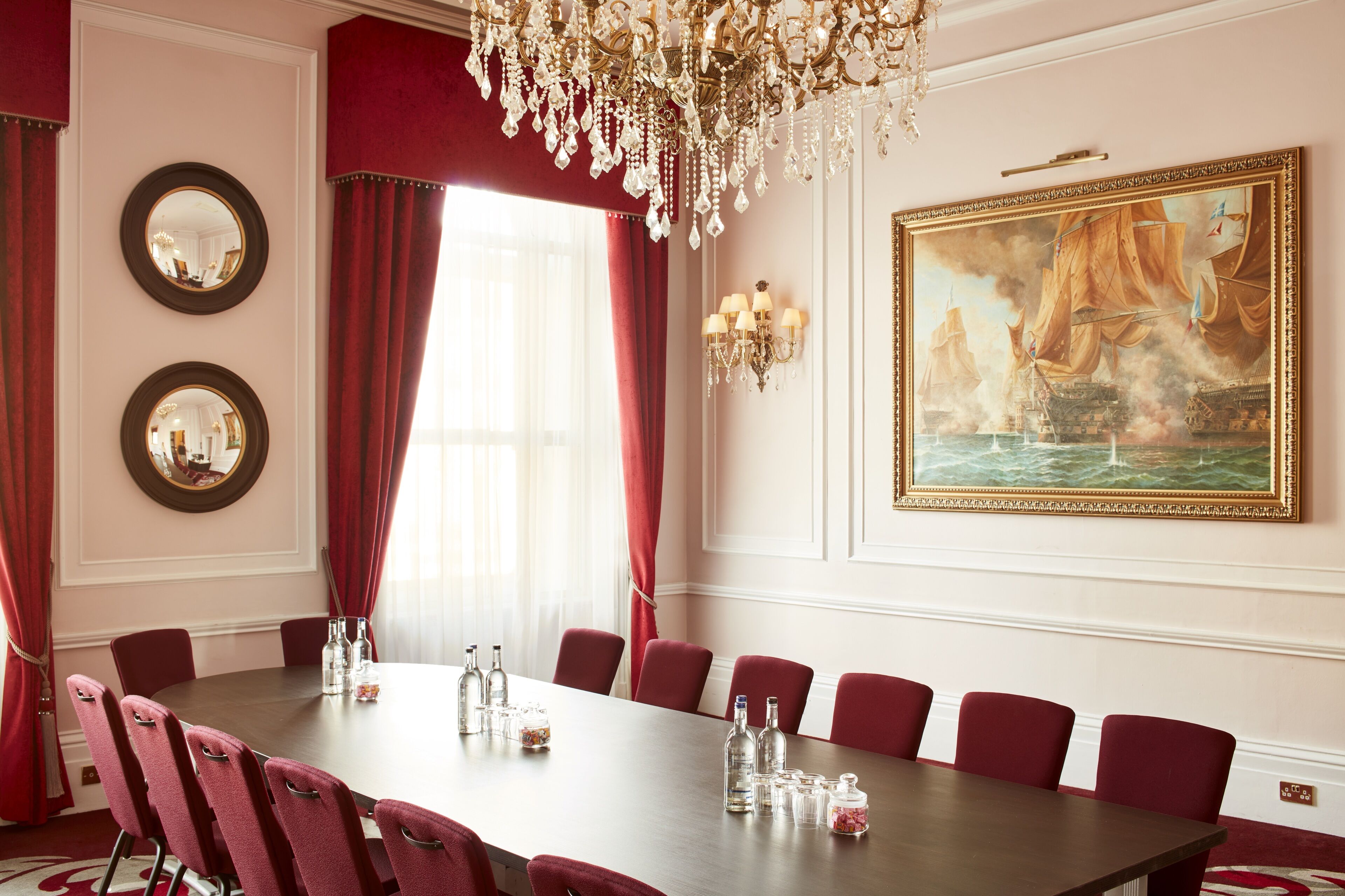 A conference room with a long table, red chairs, and a chandelier.