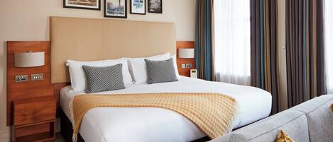 Quarto de hotel com uma cama grande, duas mesas de cabeceira, um sofá e três quadros na parede.