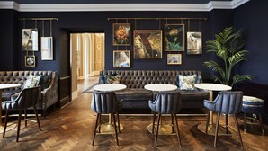 A modern lounge area with a tufted sofa, round tables, and chairs, featuring artwork on the walls. - The Clermont London, Charing Cross (London)