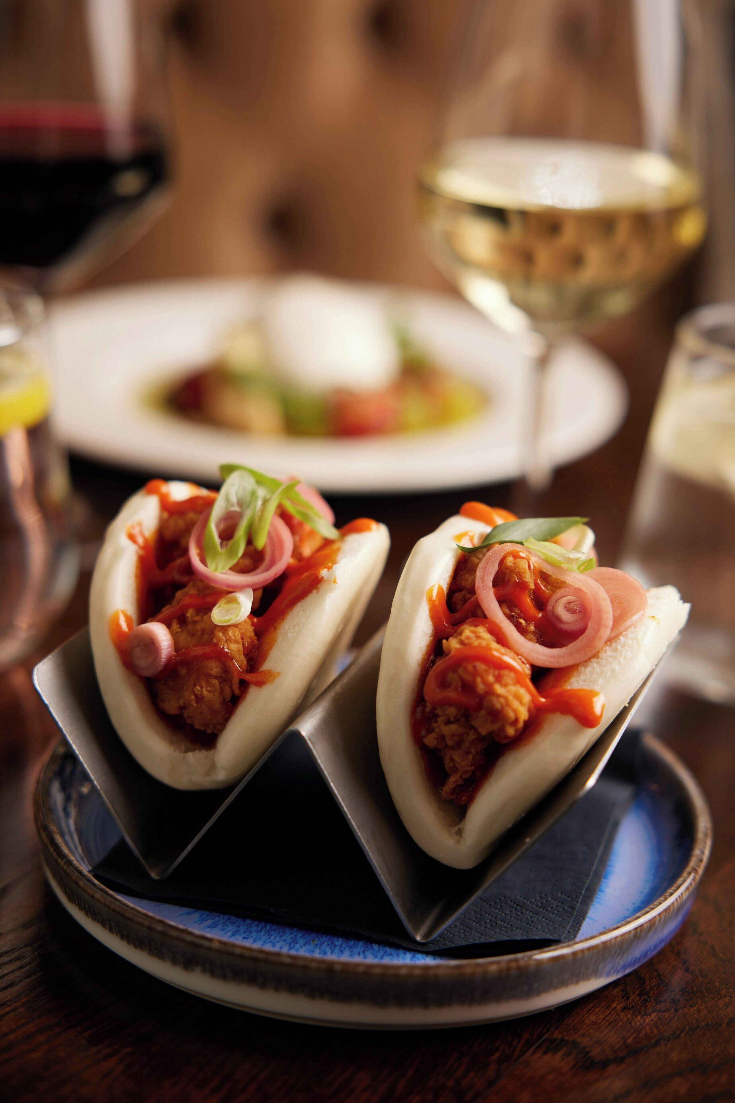 Two food items on a plate, possibly a type of sandwich or bun, with visible toppings like onions and greens.