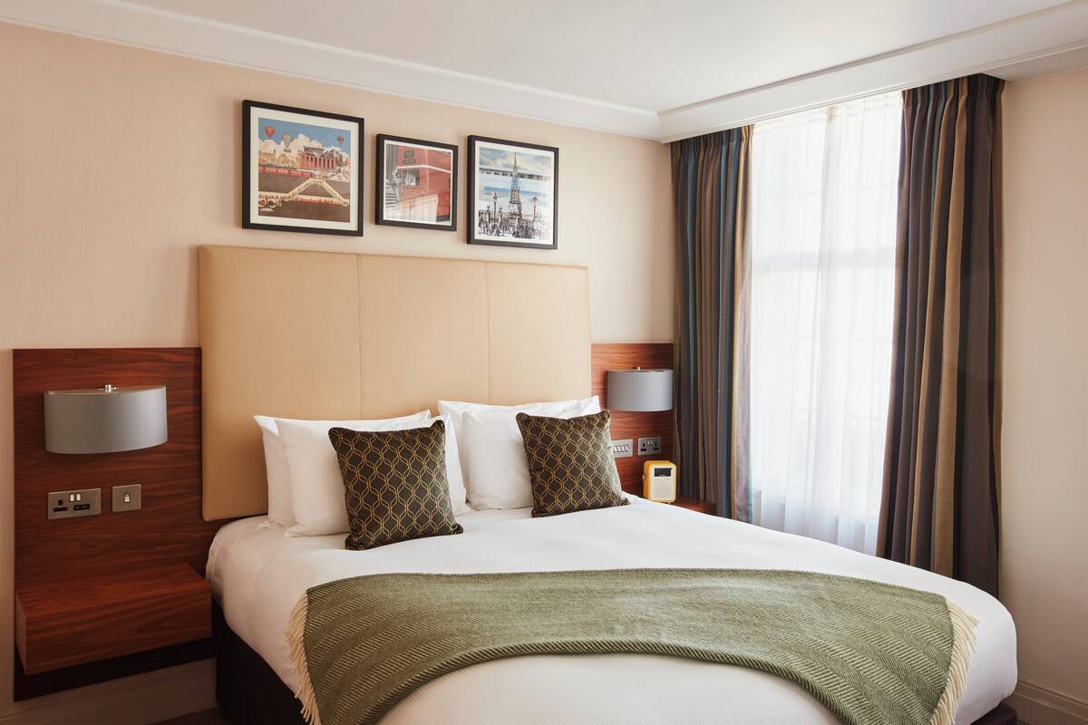 A hotel room with a large bed, two wall-mounted lamps, and framed pictures on the wall.
