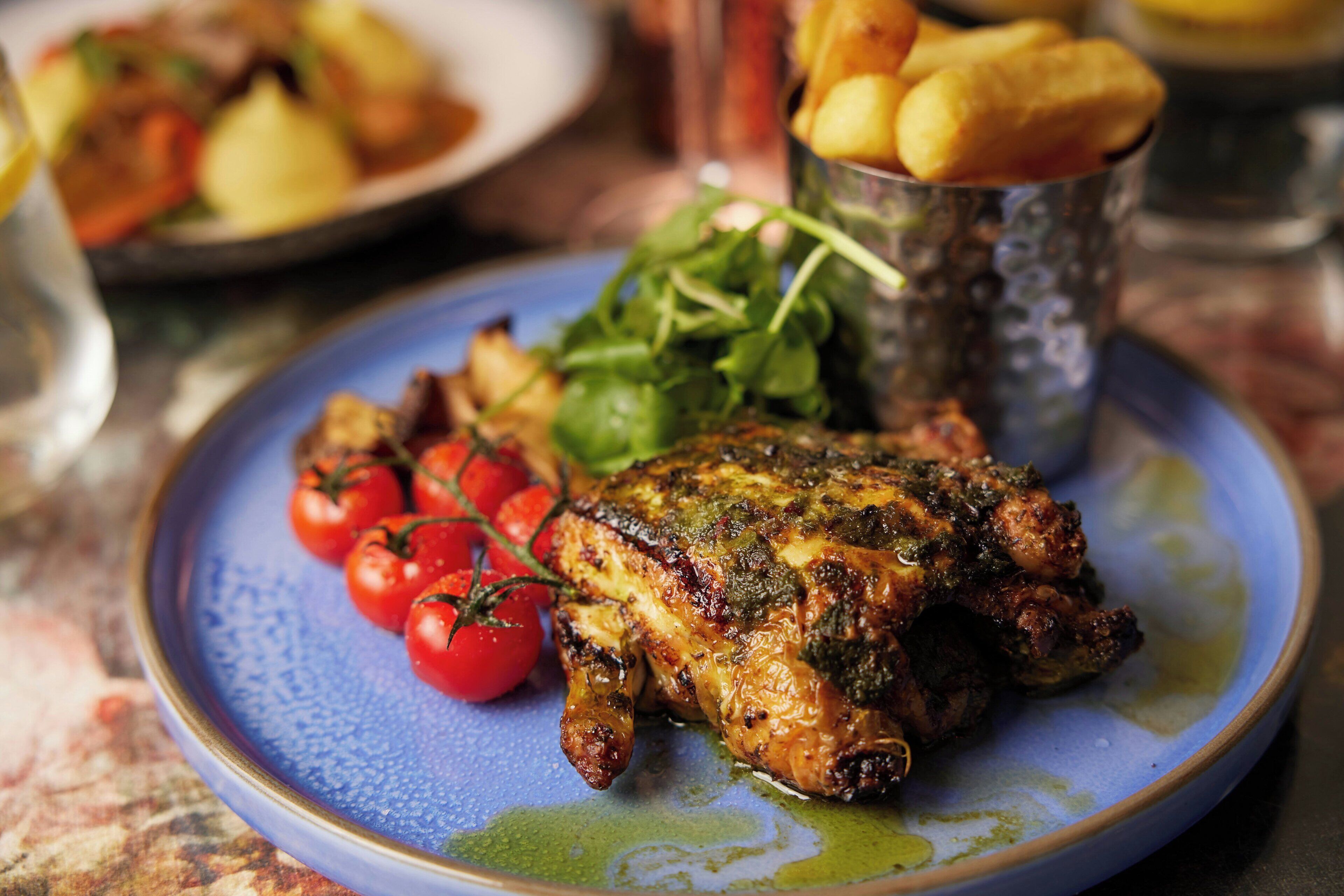 Ein Teller mit gegrilltem Hähnchen, Cocktailtomaten und Salat, dazu Pommes.