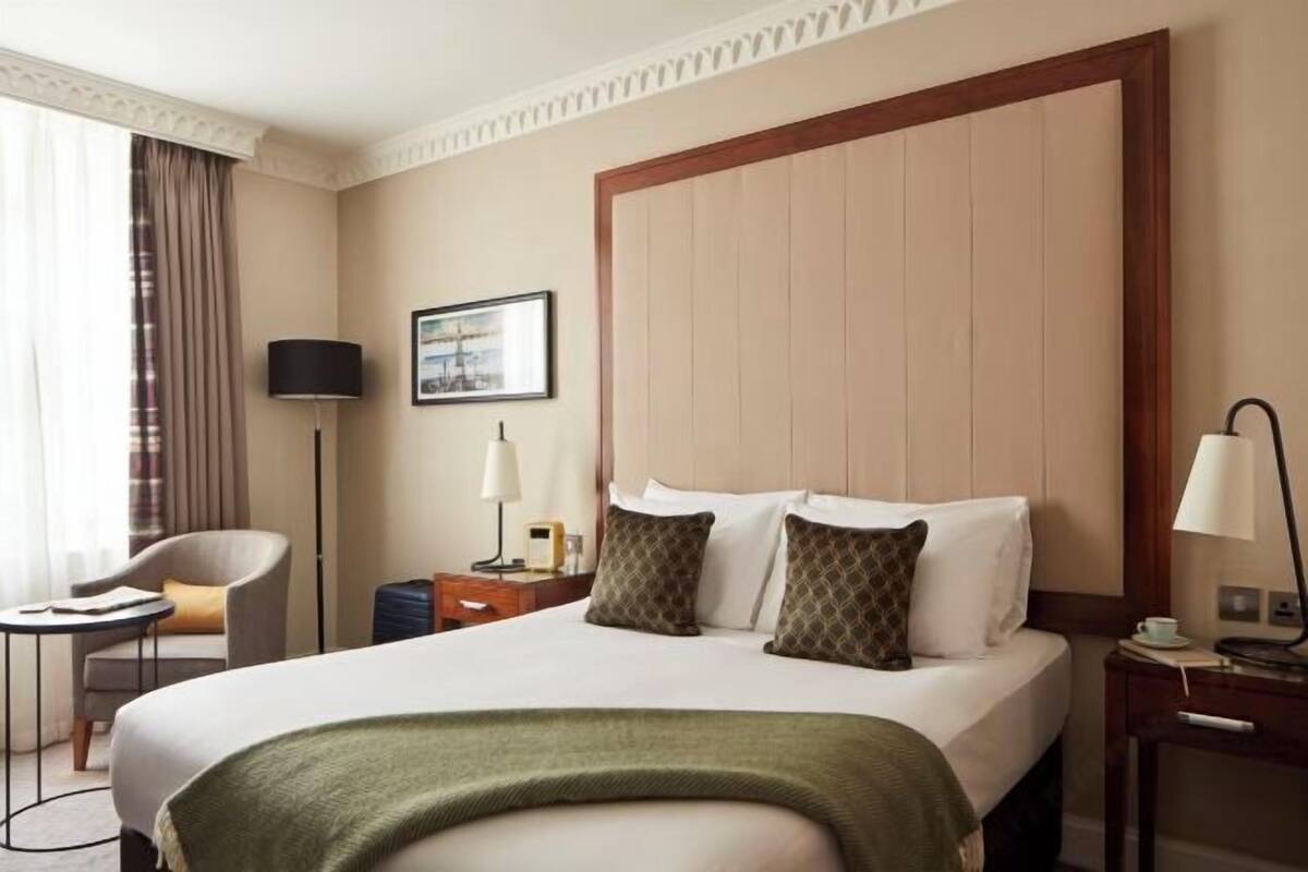 A hotel room with a large bed, a desk, a chair, a lamp, and a picture on the wall.