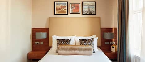 A hotel room with a large bed, two bedside tables with lamps, and three framed pictures on the wall.
