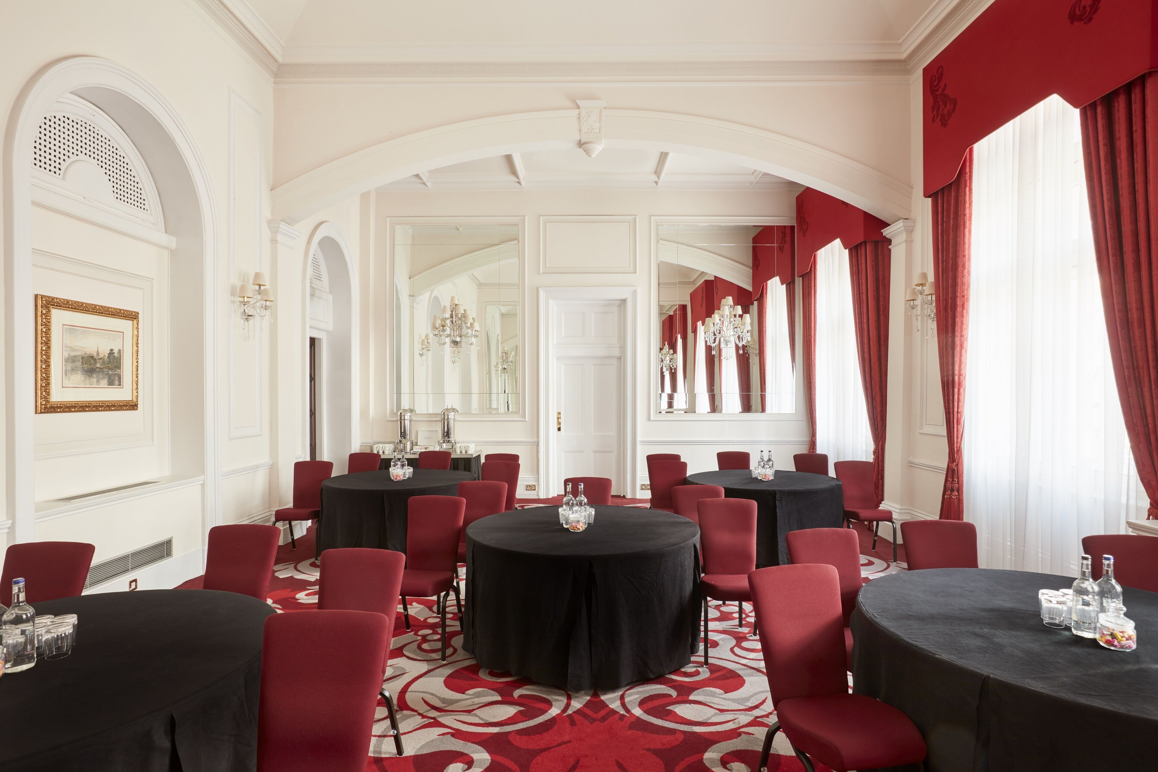 A formal conference room with multiple round tables, red chairs, and a red carpet.