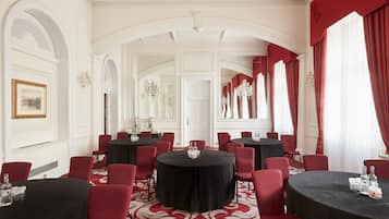 Un salón de conferencias formal con varias mesas redondas, sillas rojas y una alfombra roja.