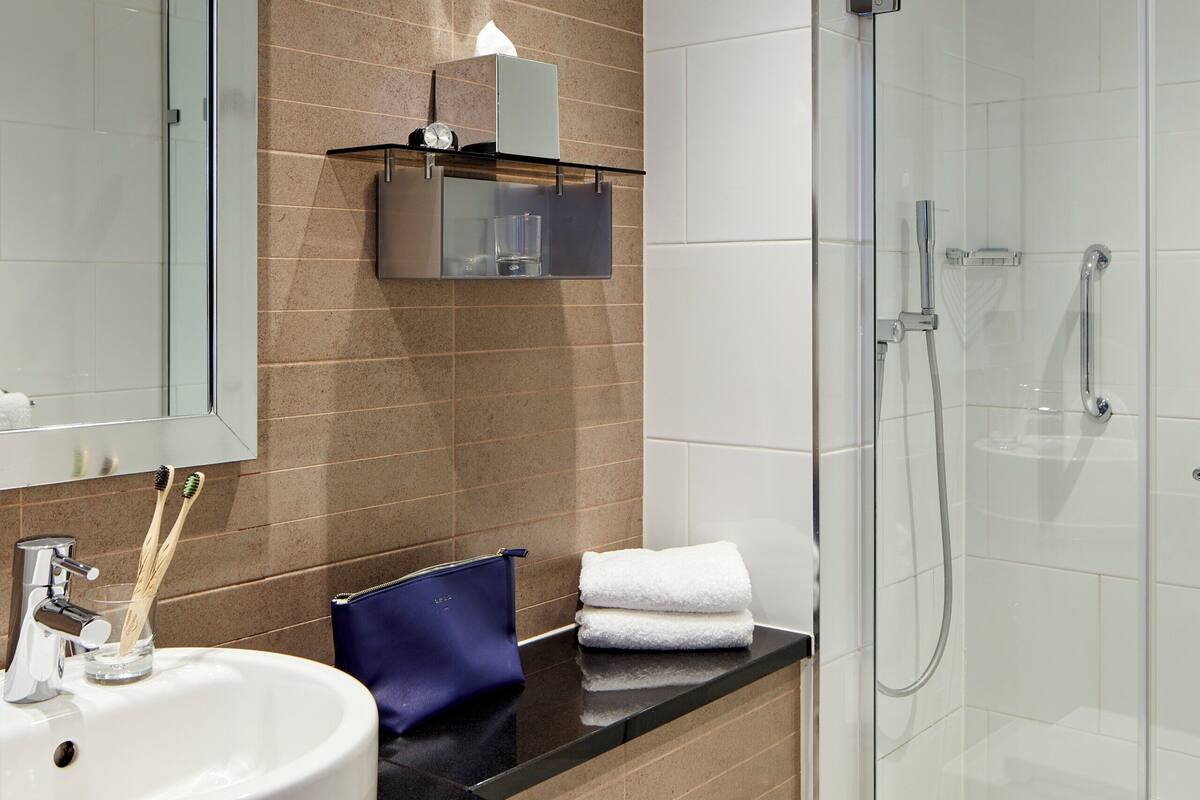 A modern bathroom with a glass-enclosed shower, a white sink, and a mirror above it.