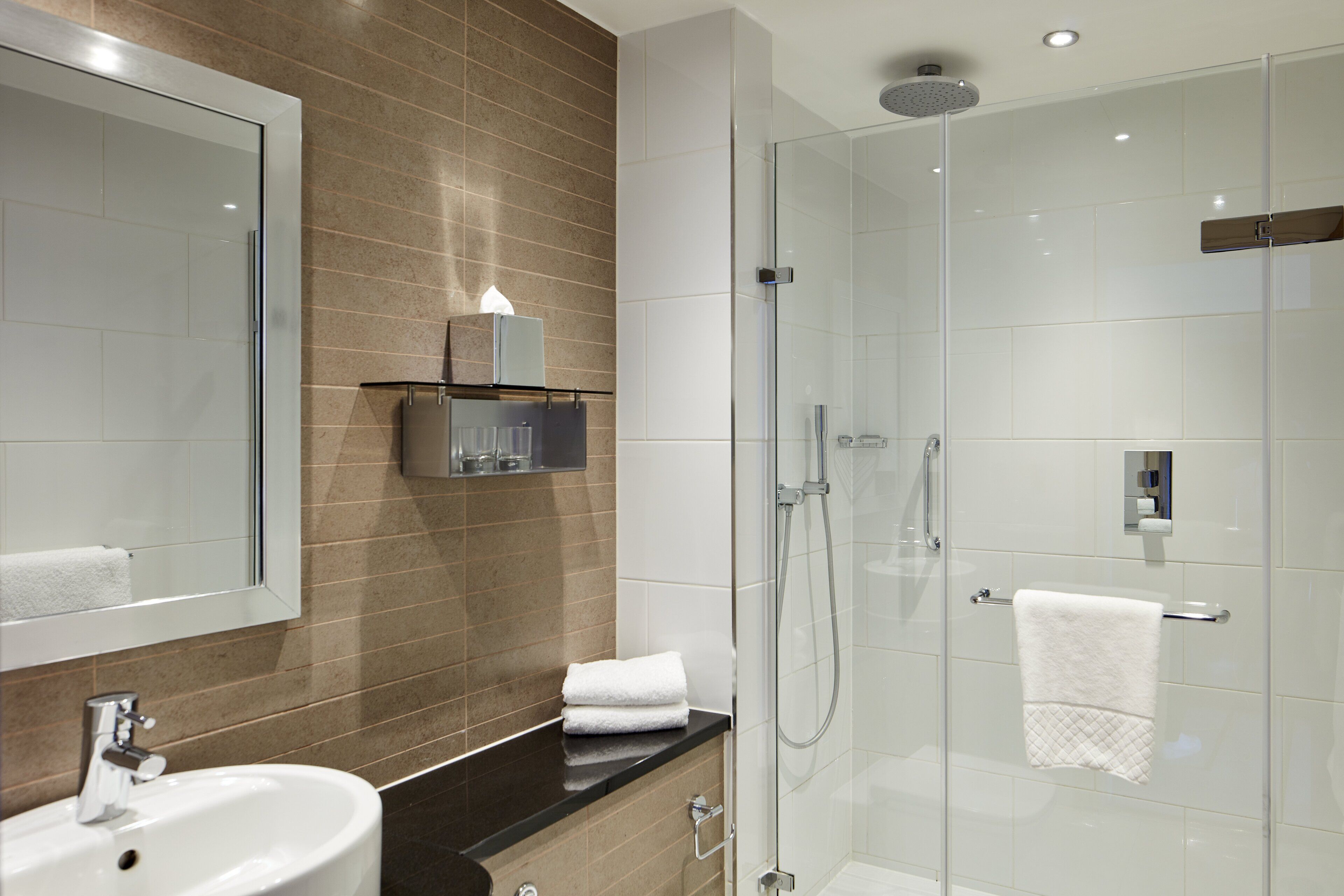 A modern bathroom with a glass-enclosed shower, a sink, and a mirror.
