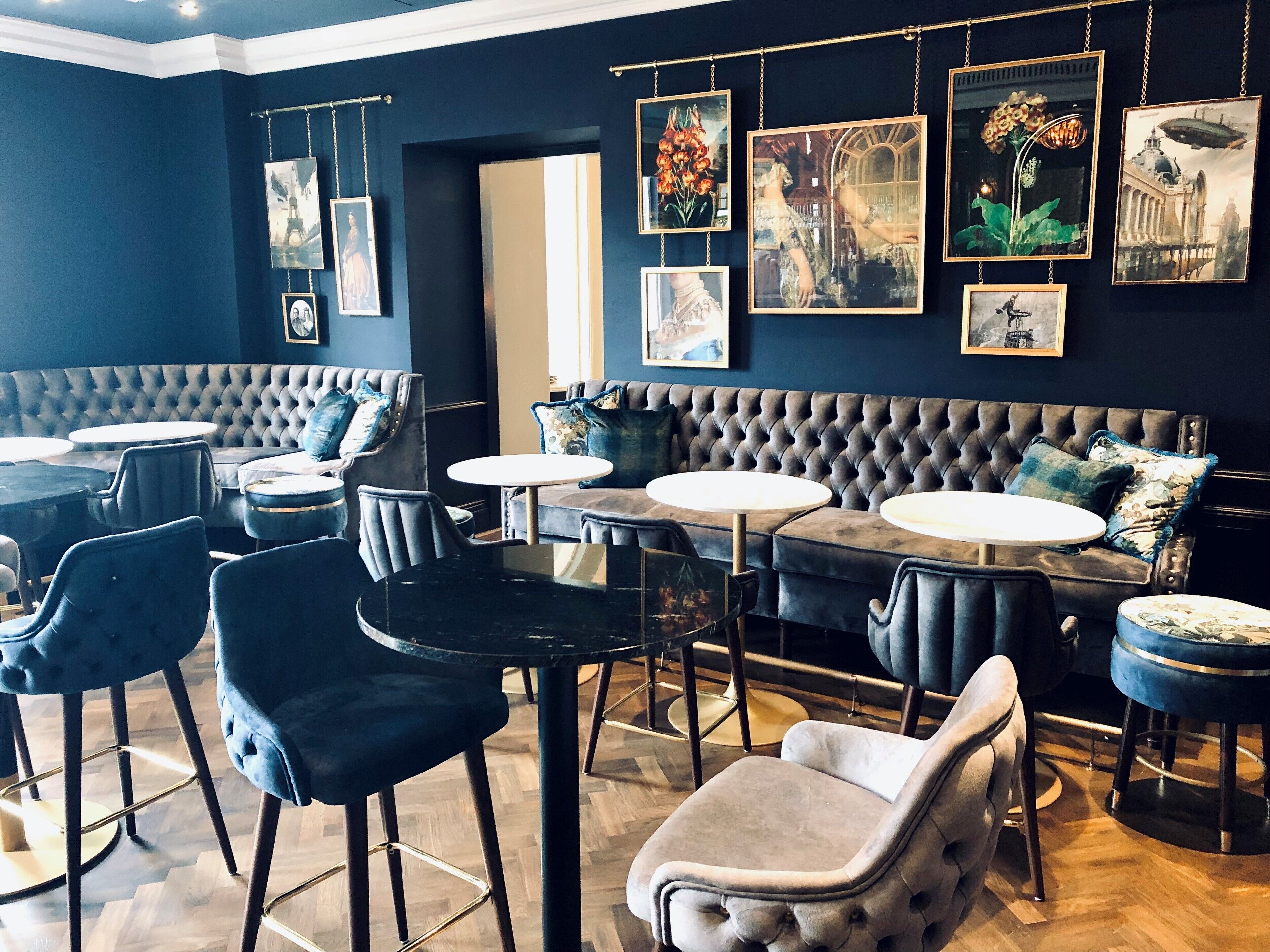 A restaurant interior with a dark blue wall, a tufted sofa, round tables, and chairs.
