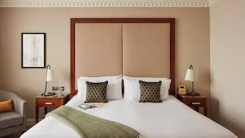 A hotel room with a large bed, two bedside tables, a chair, a framed picture on the wall, and a decorative ceiling medallion.