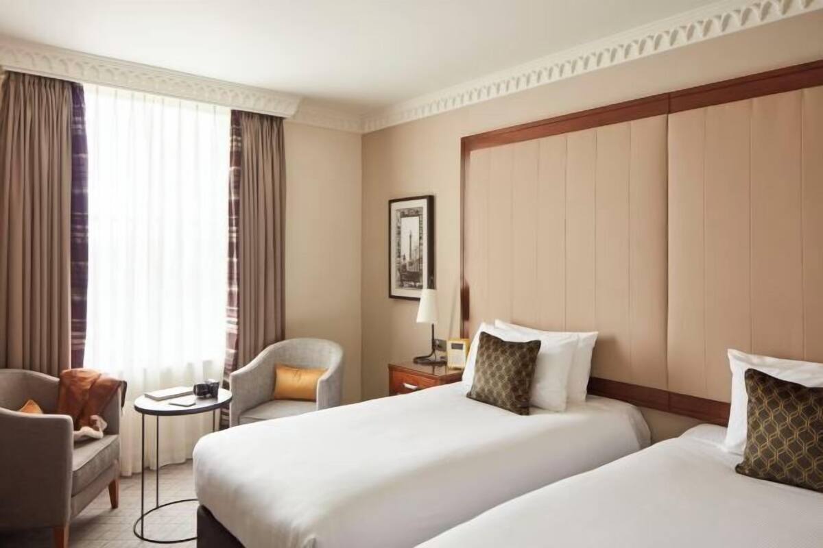 A hotel room with two beds, a sofa, a small table, and a window with curtains.