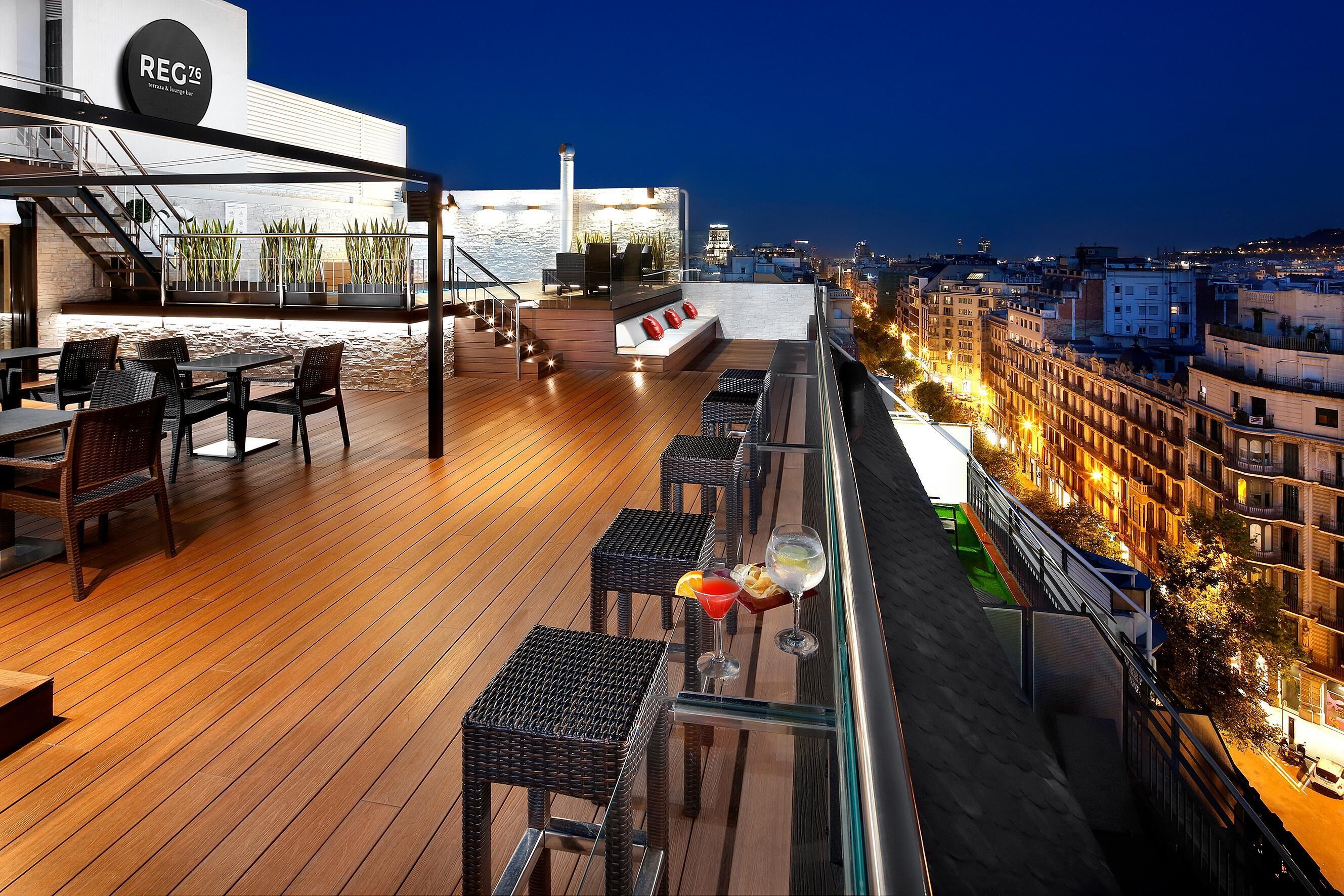 A rooftop terrace with wooden flooring, outdoor seating, and a city view at dusk.