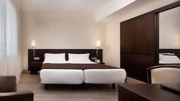 Ein Hotelzimmer mit einem Doppelbett, zwei Nachttischen, einem Schreibtisch, einem Sessel und einem großen Spiegel.