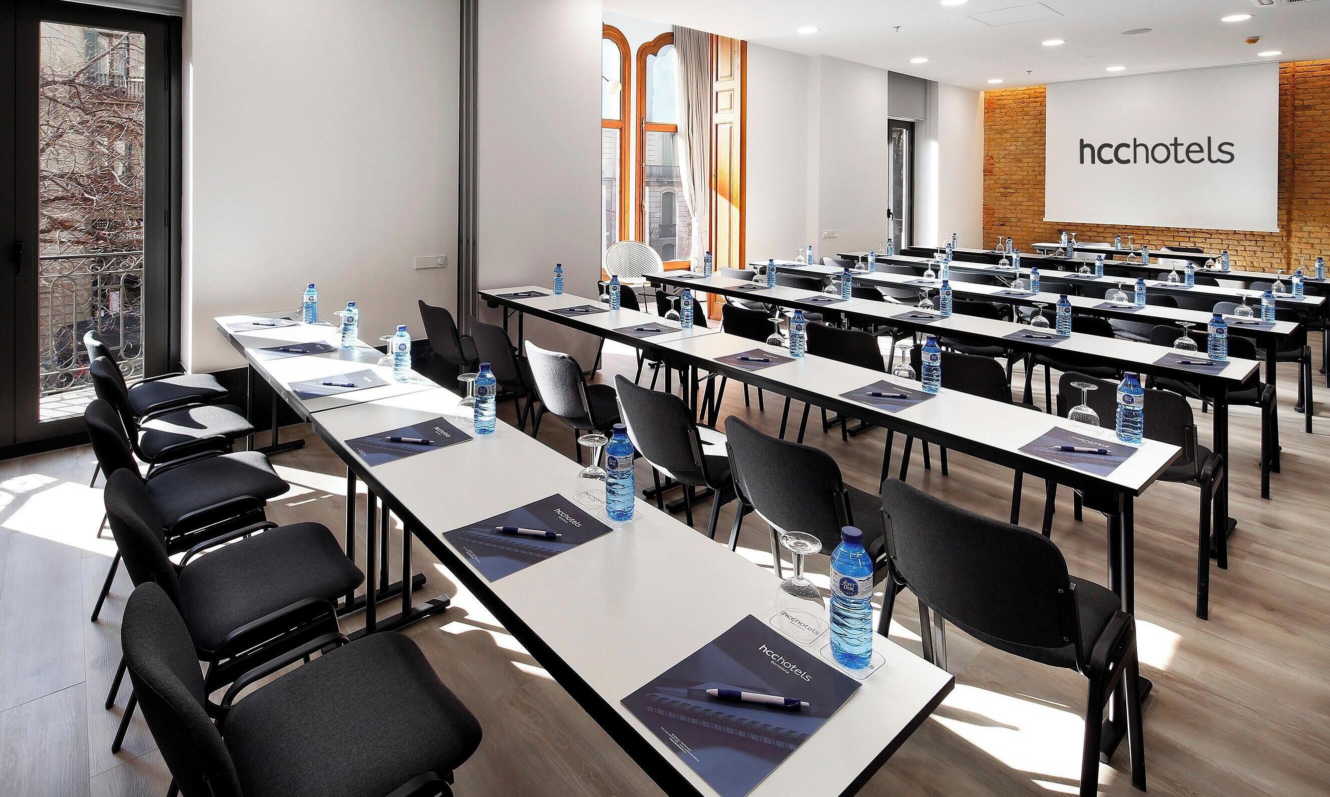 A conference room with multiple tables, chairs, water bottles, and a presentation screen.