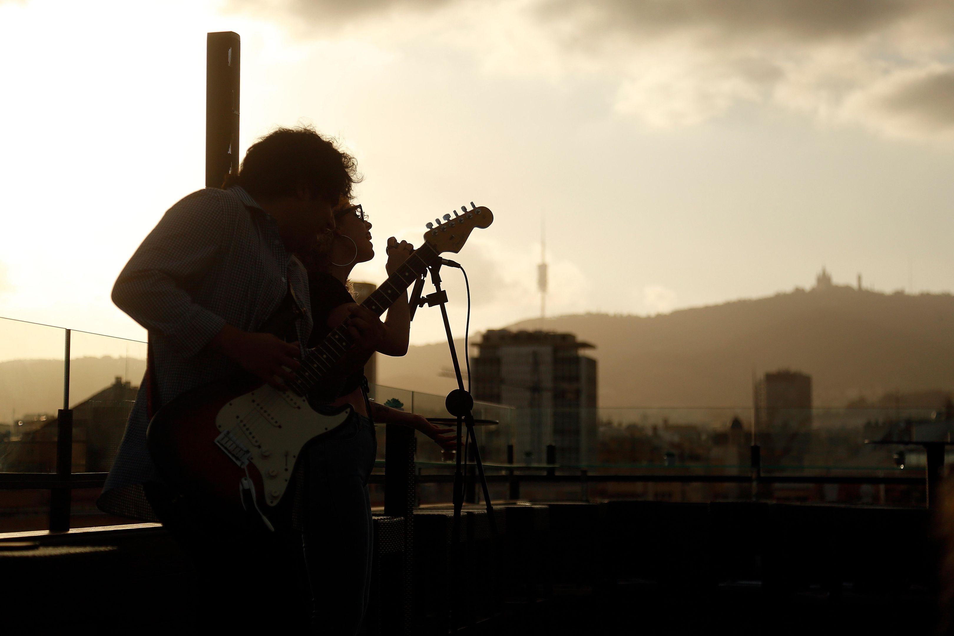 Una persona tocando la guitarra en un tejado con un paisaje urbano de fondo.