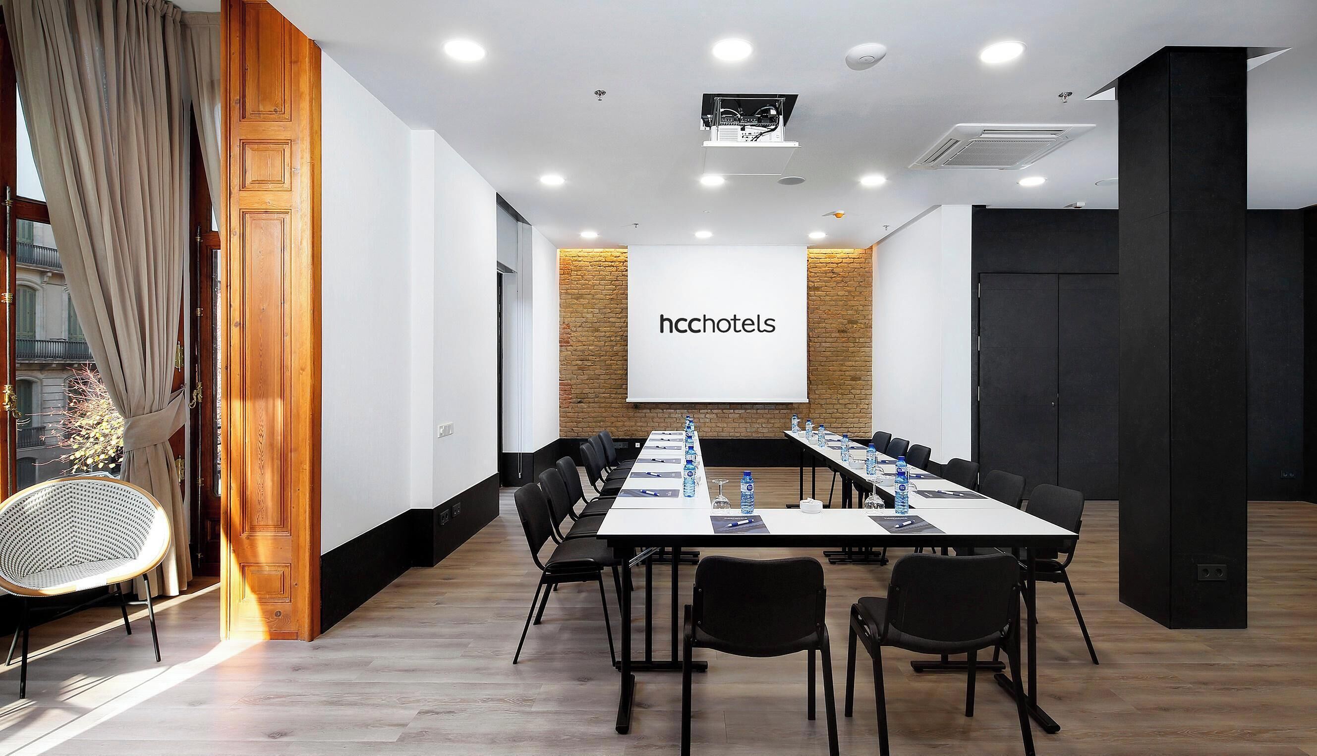 A conference room with a long table, chairs, a projector screen, and a brick wall.