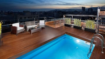 Una piscina sul tetto con pavimento in legno, mobili in vimini e piante in vaso.