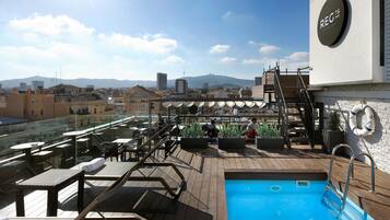 A rooftop pool area with a view of the city and mountains in the background.