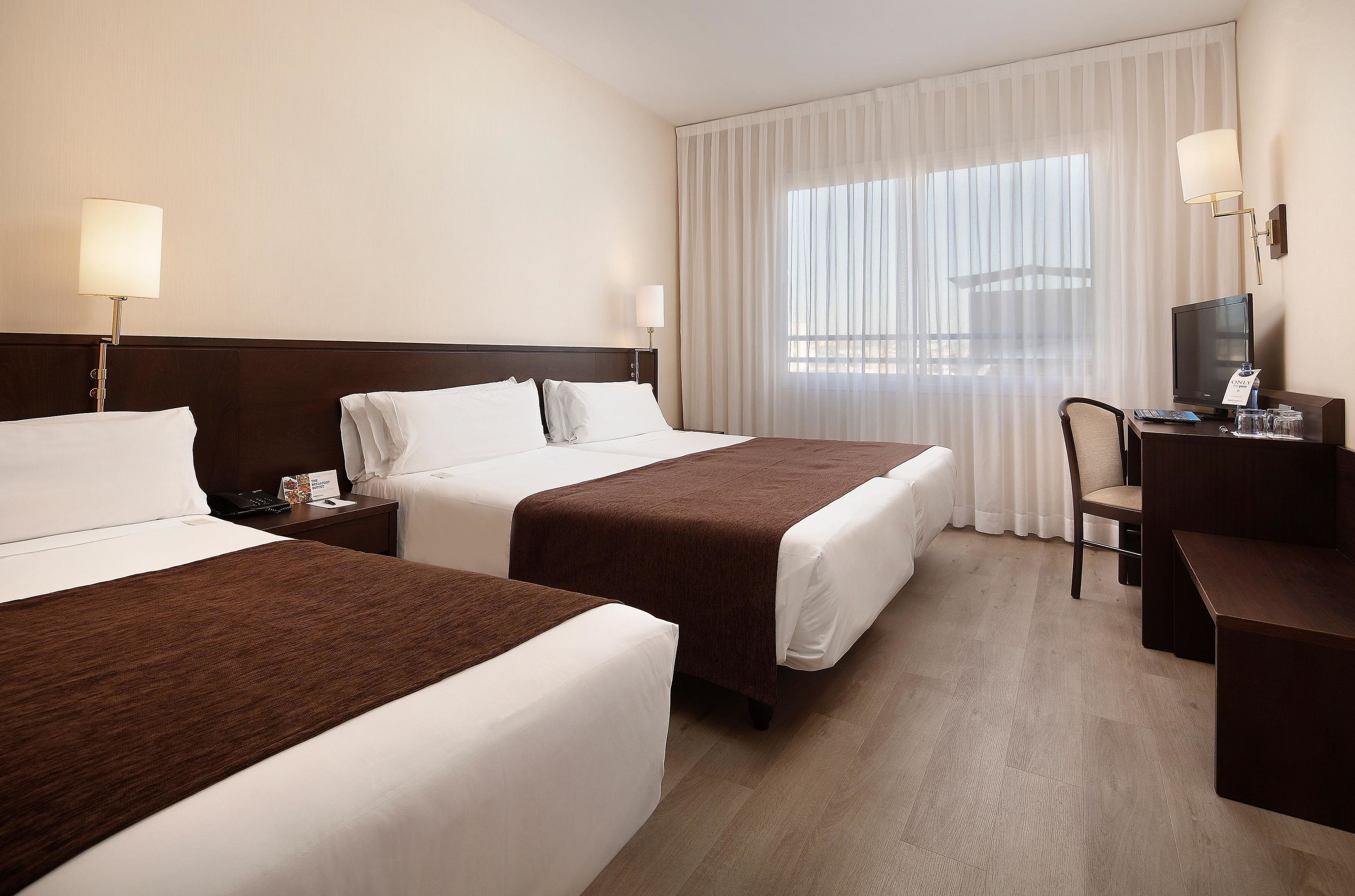 Een hotelkamer met twee bedden, een bureau met stoel, een televisie en een raam met gordijnen.