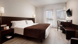 A hotel room with a bed, a desk, a chair, a TV, and a nightstand. - Hotel HCC Regente (Barcelona)