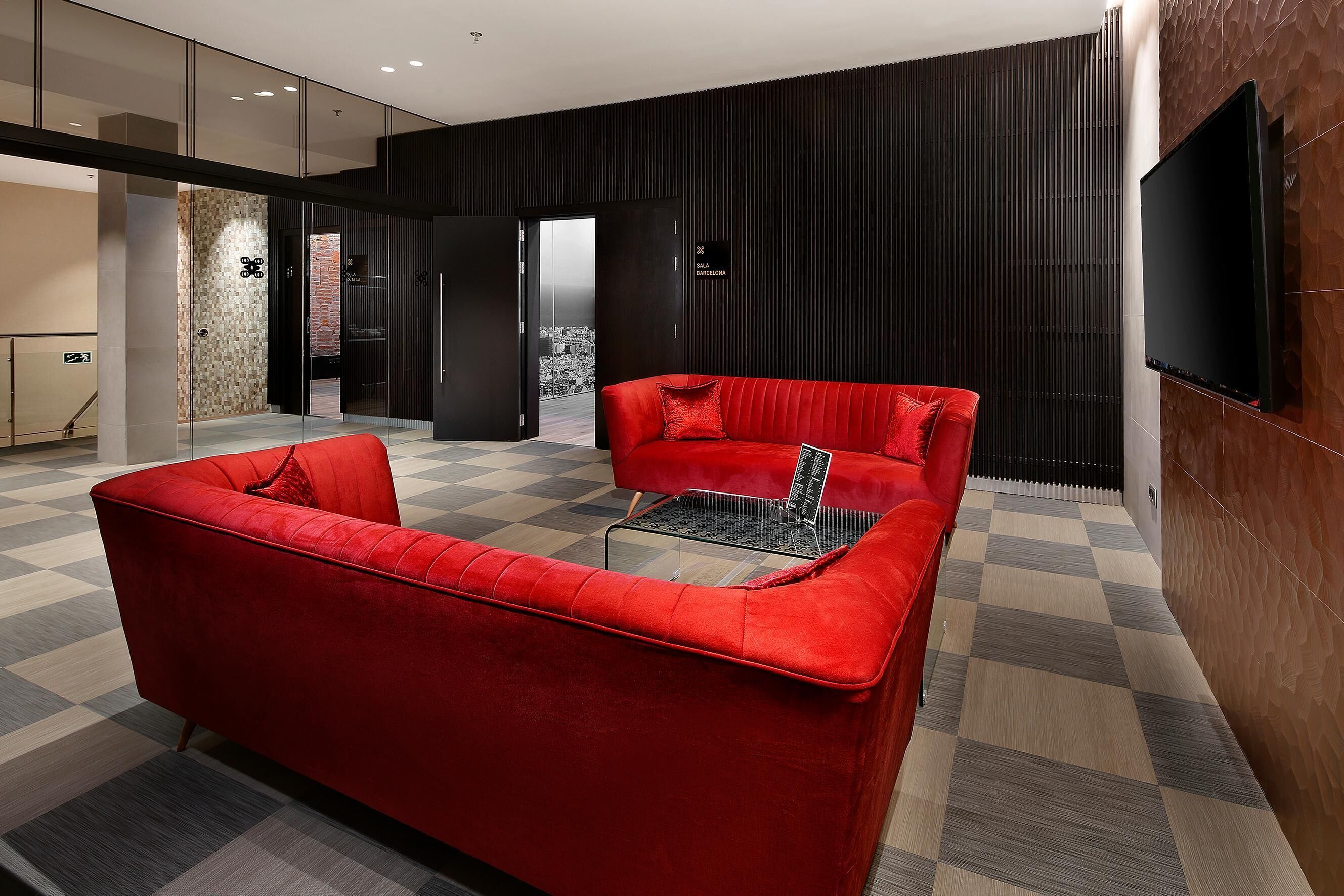 A modern lobby with a red sofa set, a glass coffee table, and a flat-screen TV mounted on the wall.